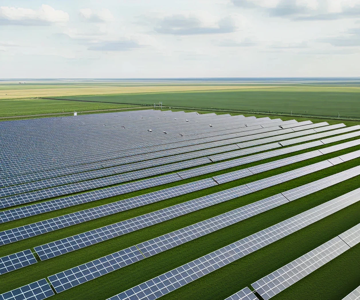 Großflächiger Solarpark mit langen Reihen von Photovoltaikmodulen auf grünen Feldern unter leicht bewölktem Himmel.